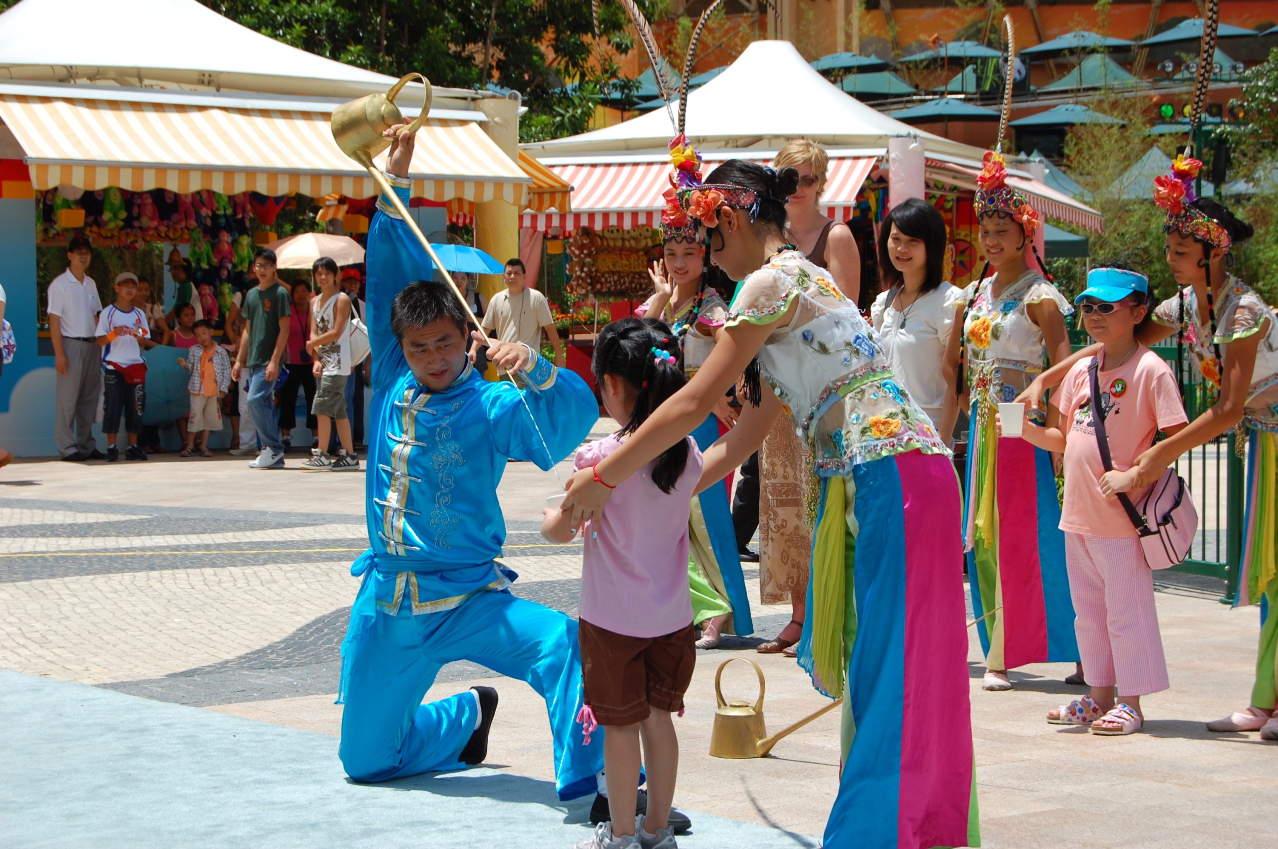 A culture show in Ocean Park, Hong Kong, featuring a man in a bright blue outfit artfully pouring tea into a cup a little girl is holding.