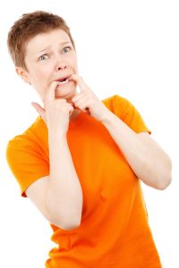 A woman in an orange shirt biting her forefingers looking nervous and scared.