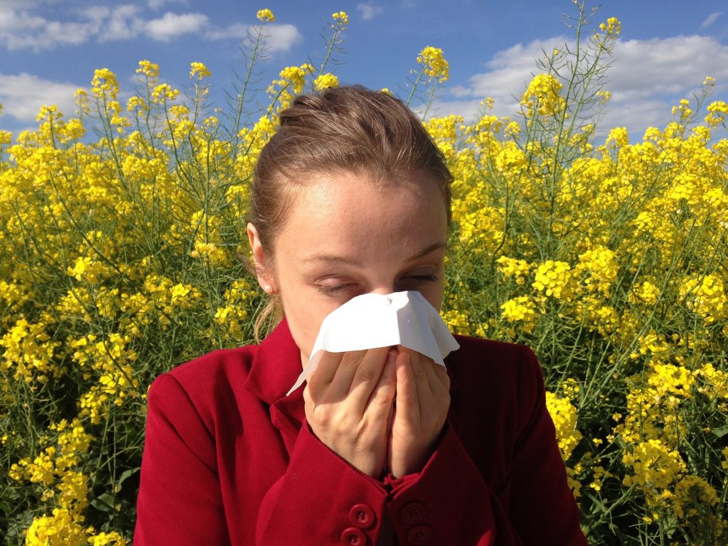 A woman with a red blazer sneezing and covering her mouth and nose with a white tissue.