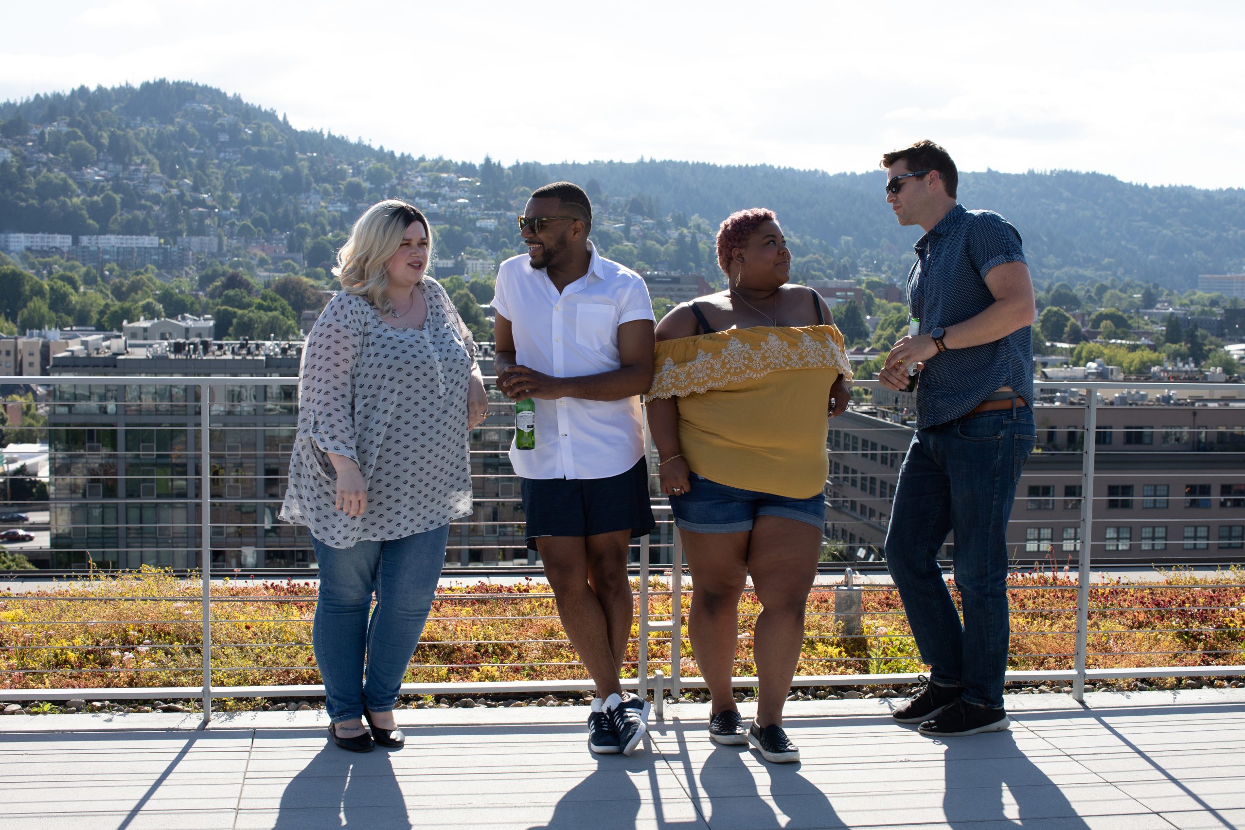 Two women talk to two men while standing against a garden roof railing.