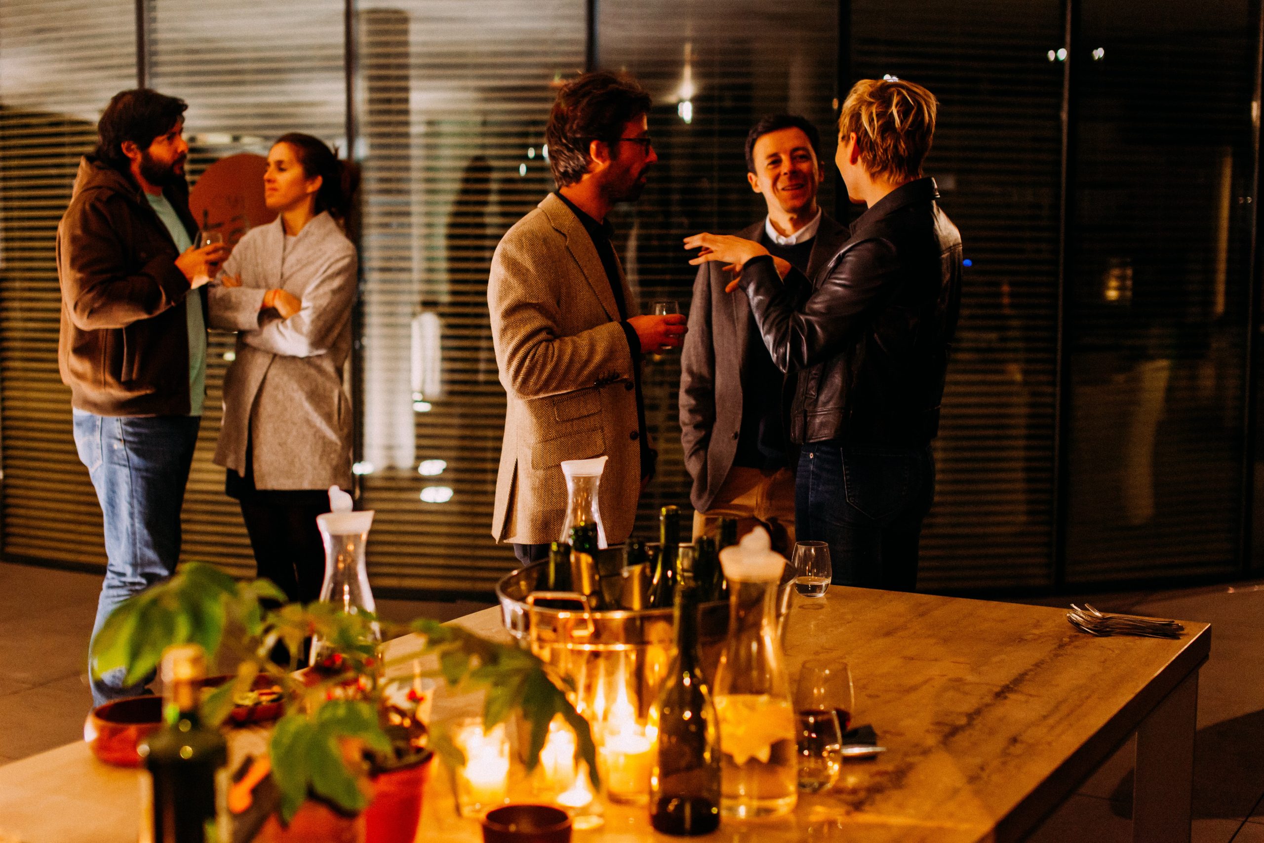 Five people standing and talking at the party. Two people holding glasses of wine.