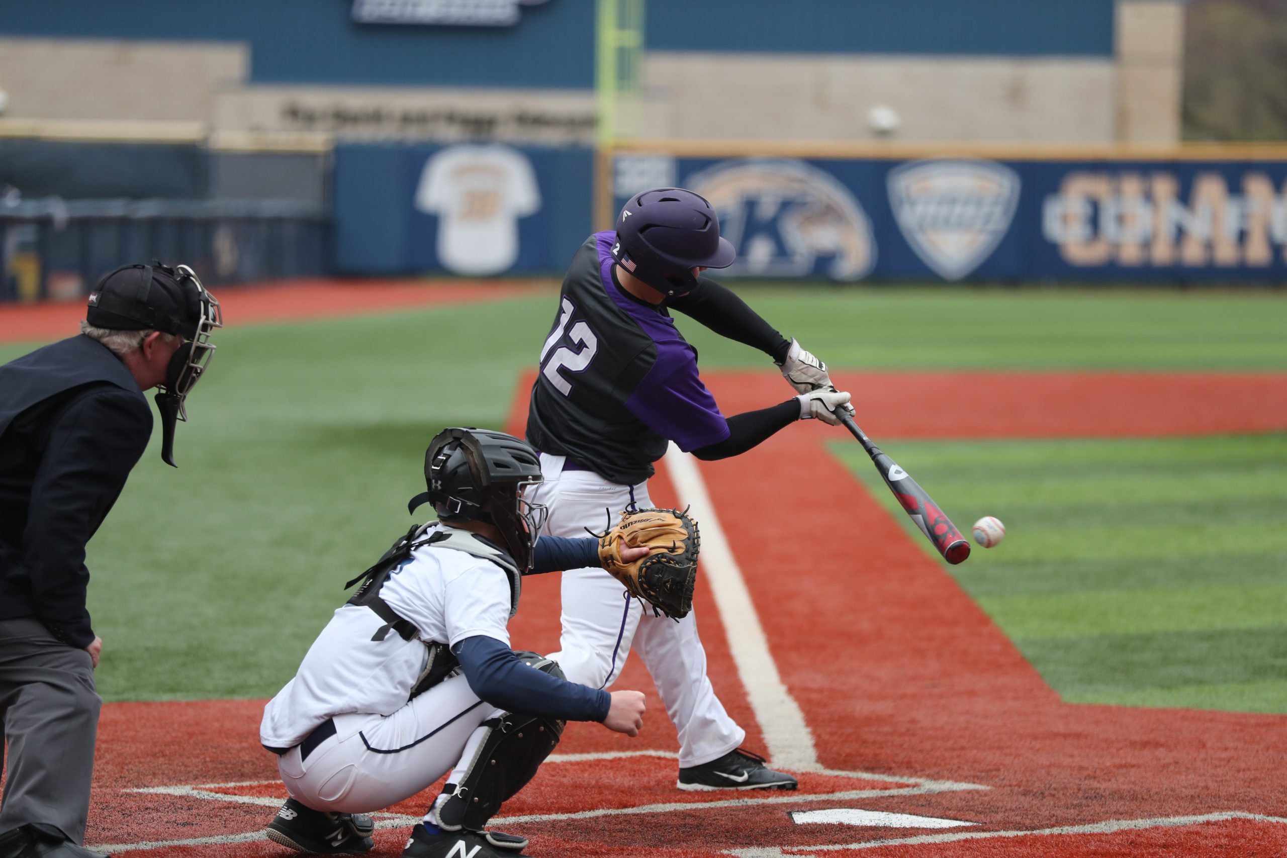 Three people are in the baseball game, one man hit the coming ball, two other men are behind him. A back catcher and a coach.