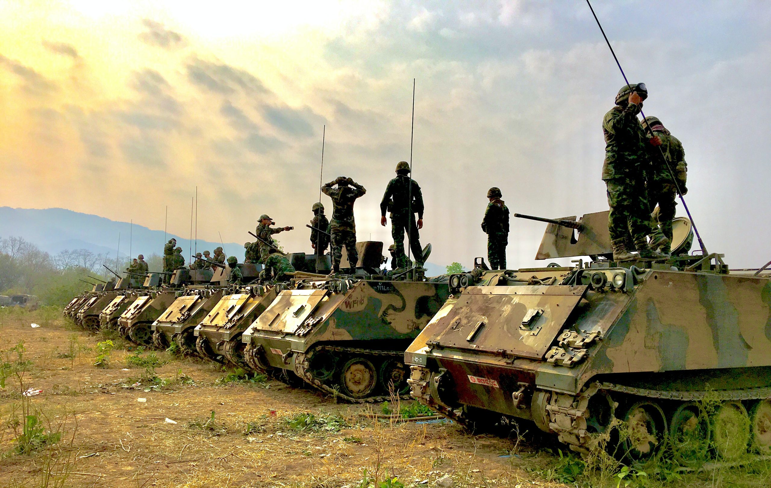 Some military tanks are arranged in line with some armies standing on top of each tanks