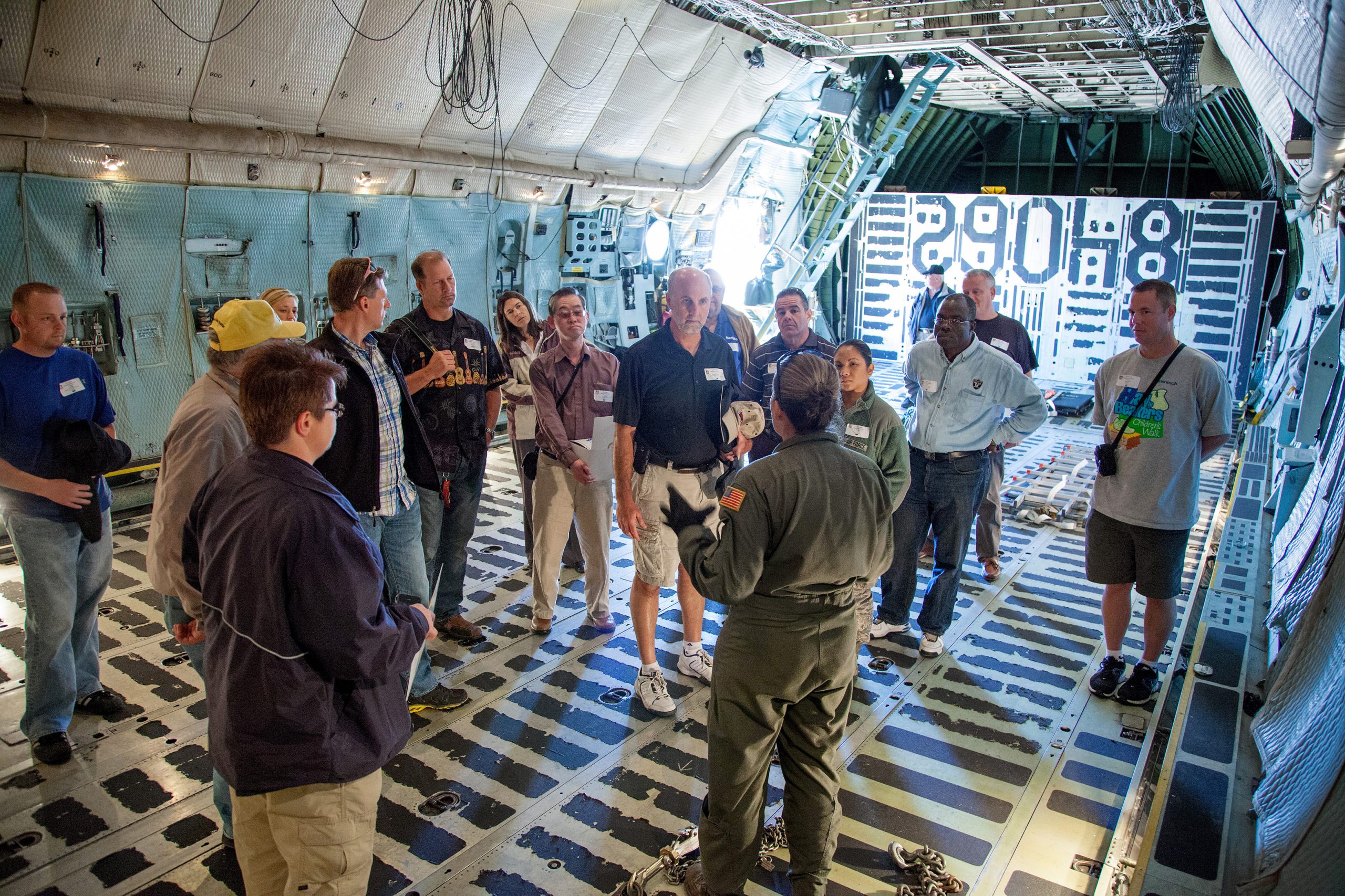 A woman in a U.S. airforce uniform talks to a group of people all standing inside of a cargo bay.