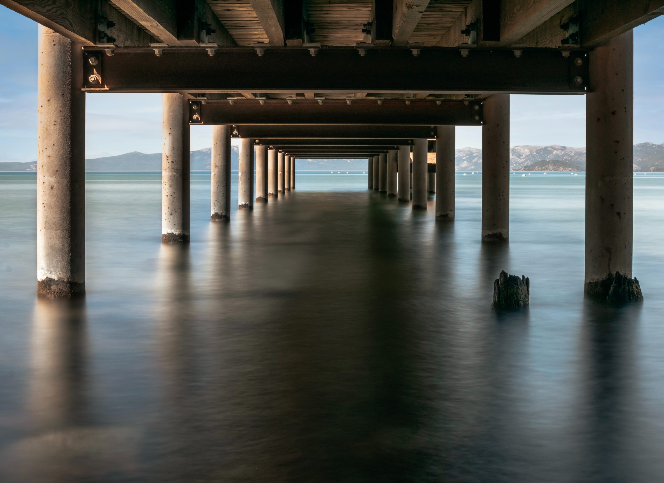 The underside of a dock with thick cylindrical pillars on either side, going into the water.