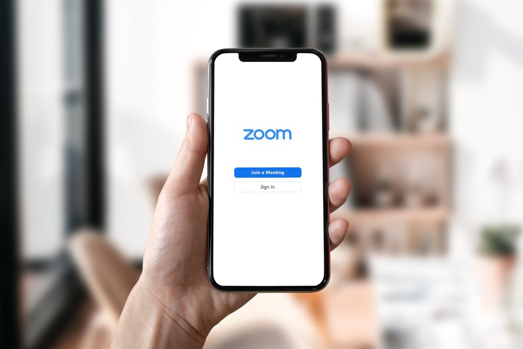 A hand holding a smartphone that displays zoom join a meeting button and sign in button on a white screen.