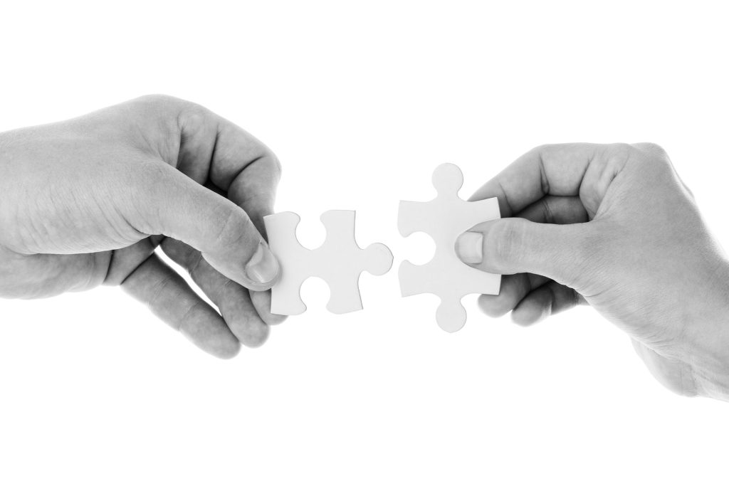 Two hands each hold a puzzle piece while bringing them to fit together.