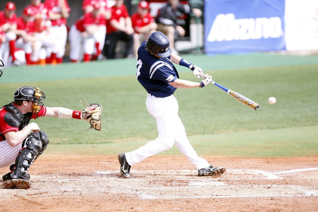 A baseball player swinging his bat at a baseball, with a catcher preparing to catch behind him.