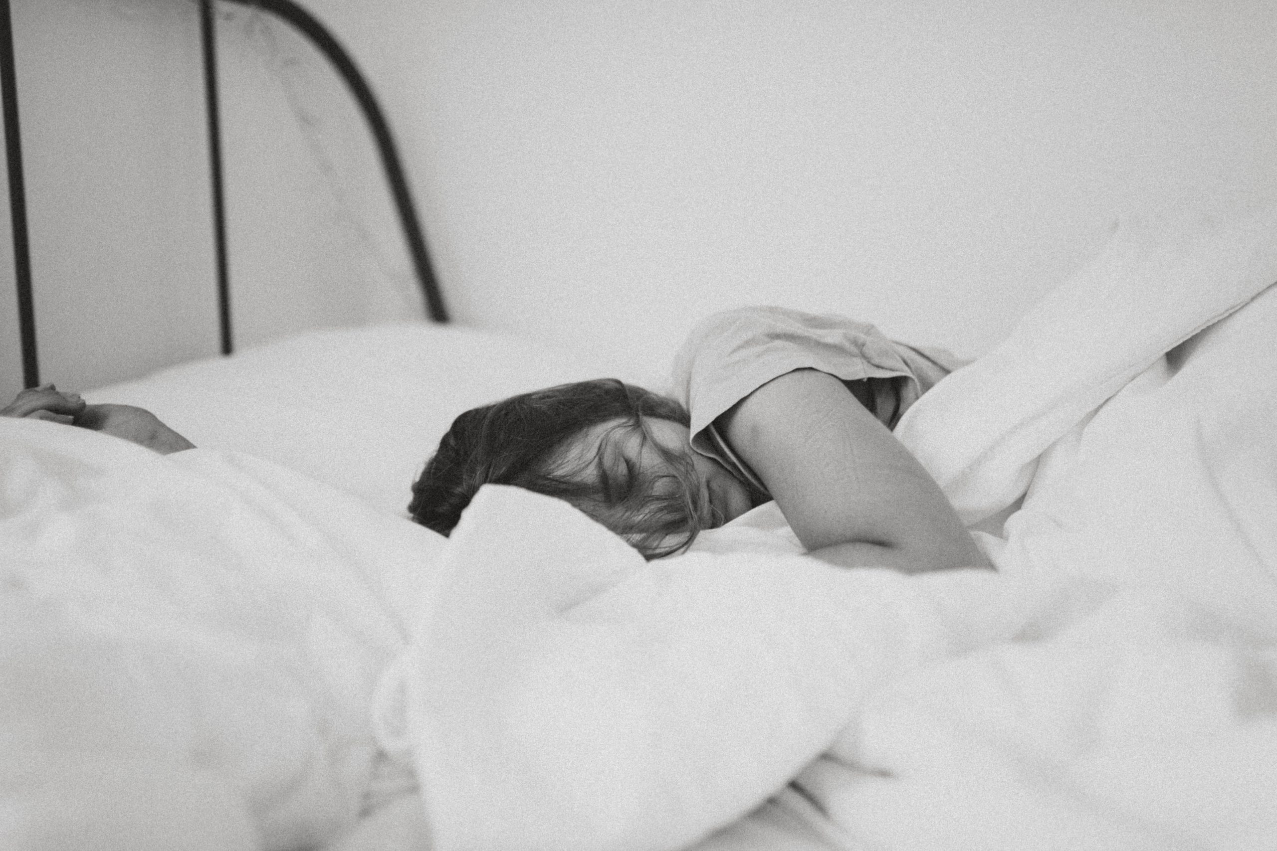 A grayscale photo of a sleeping woman lying on the bed.