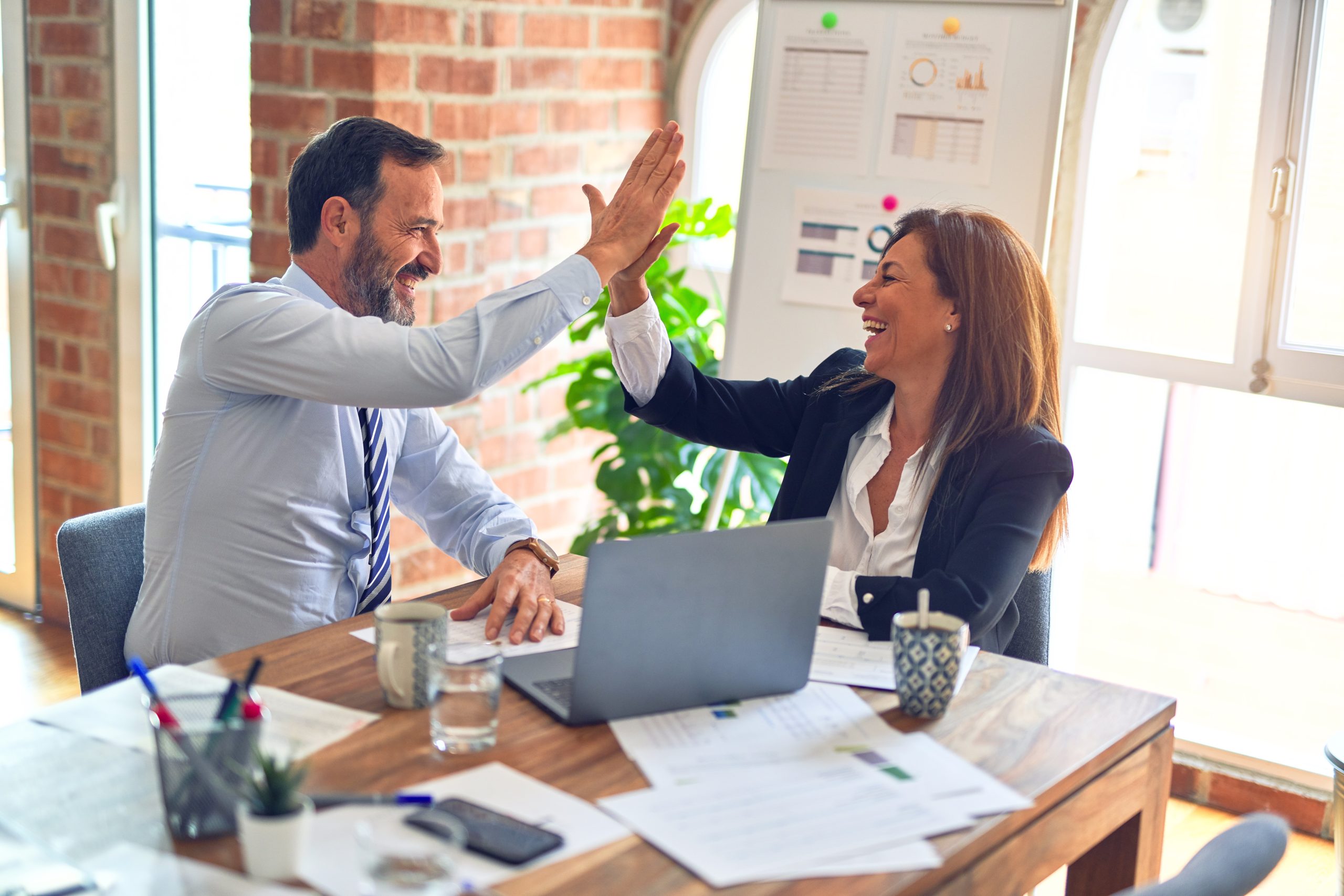 Two middle aged business workers smiling happy and confident. Working together with a smile on their faces and giving high five at the office.