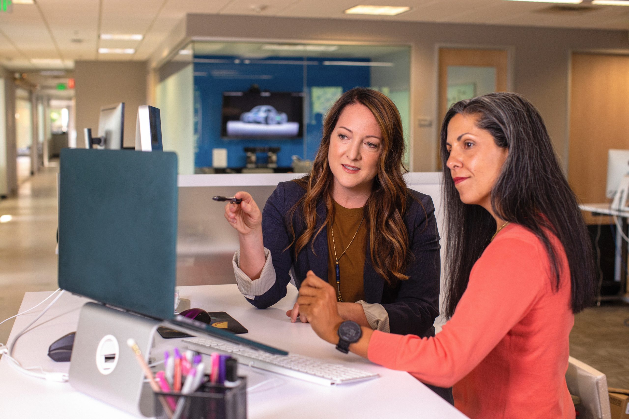 Two business women talking about sales in the office at desk with laptop.