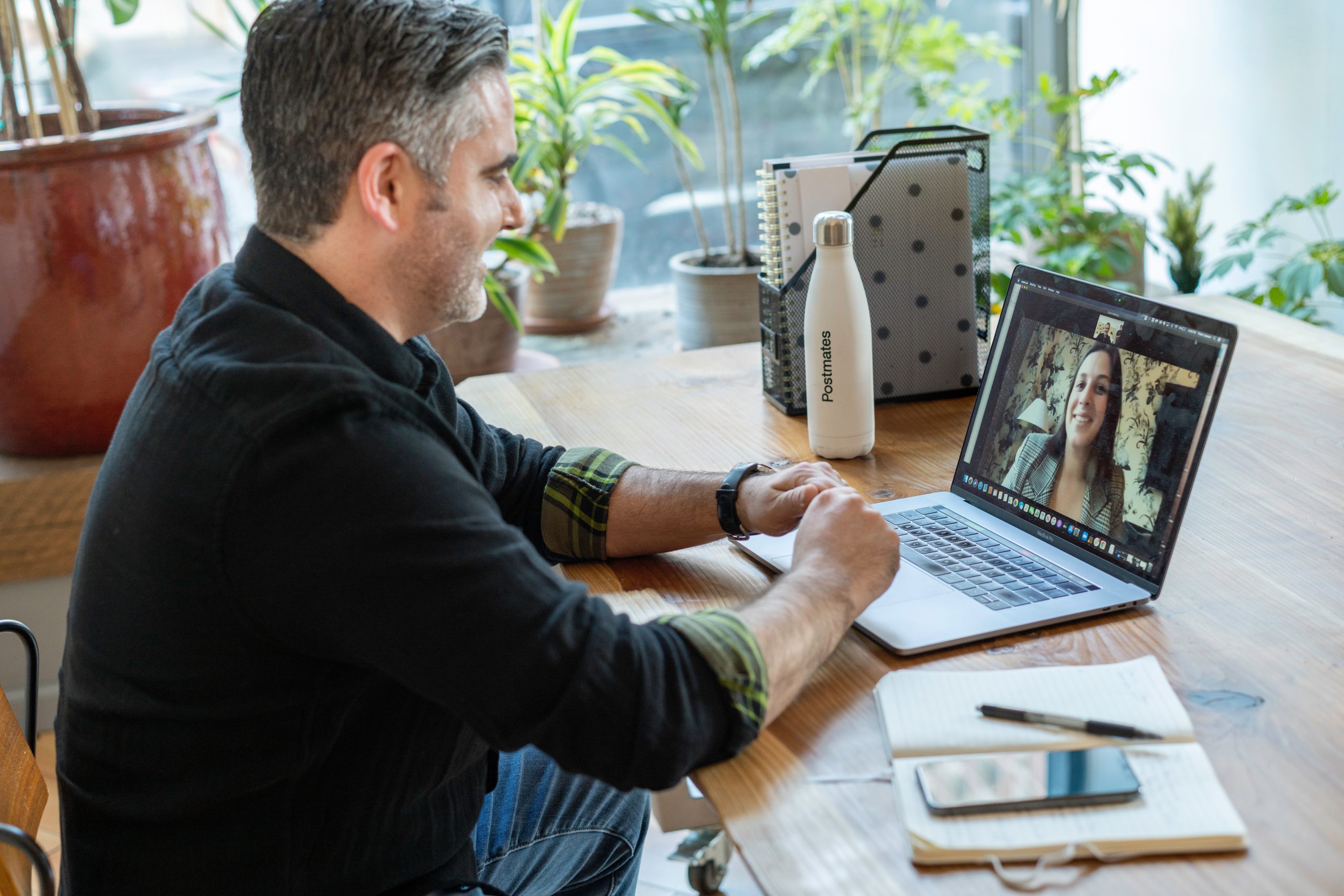 A man in a black sweater on a video conference with a woman with a gray blazer on the Macbook screen.