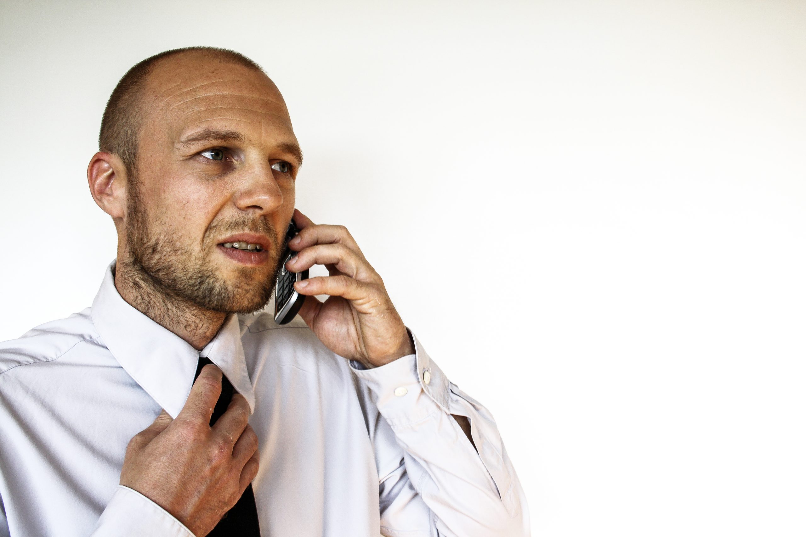 An anxious looking man talking on the phone while grabbing his tie.
