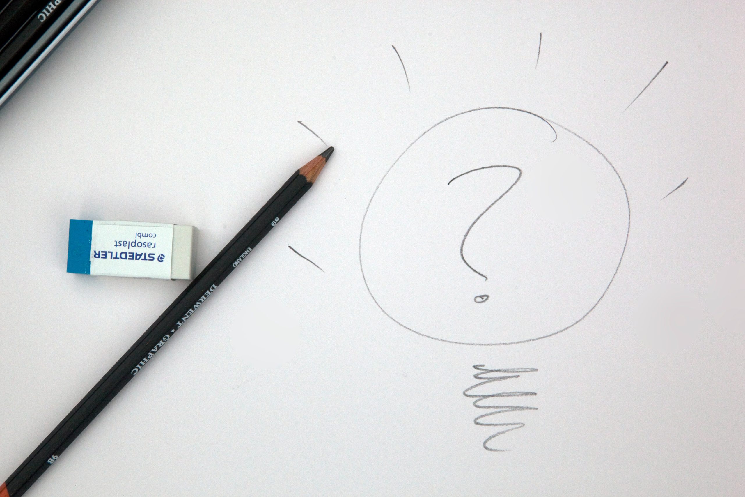 A pencil and eraser on the white paper that has a sketch of a light bulb and question mark.