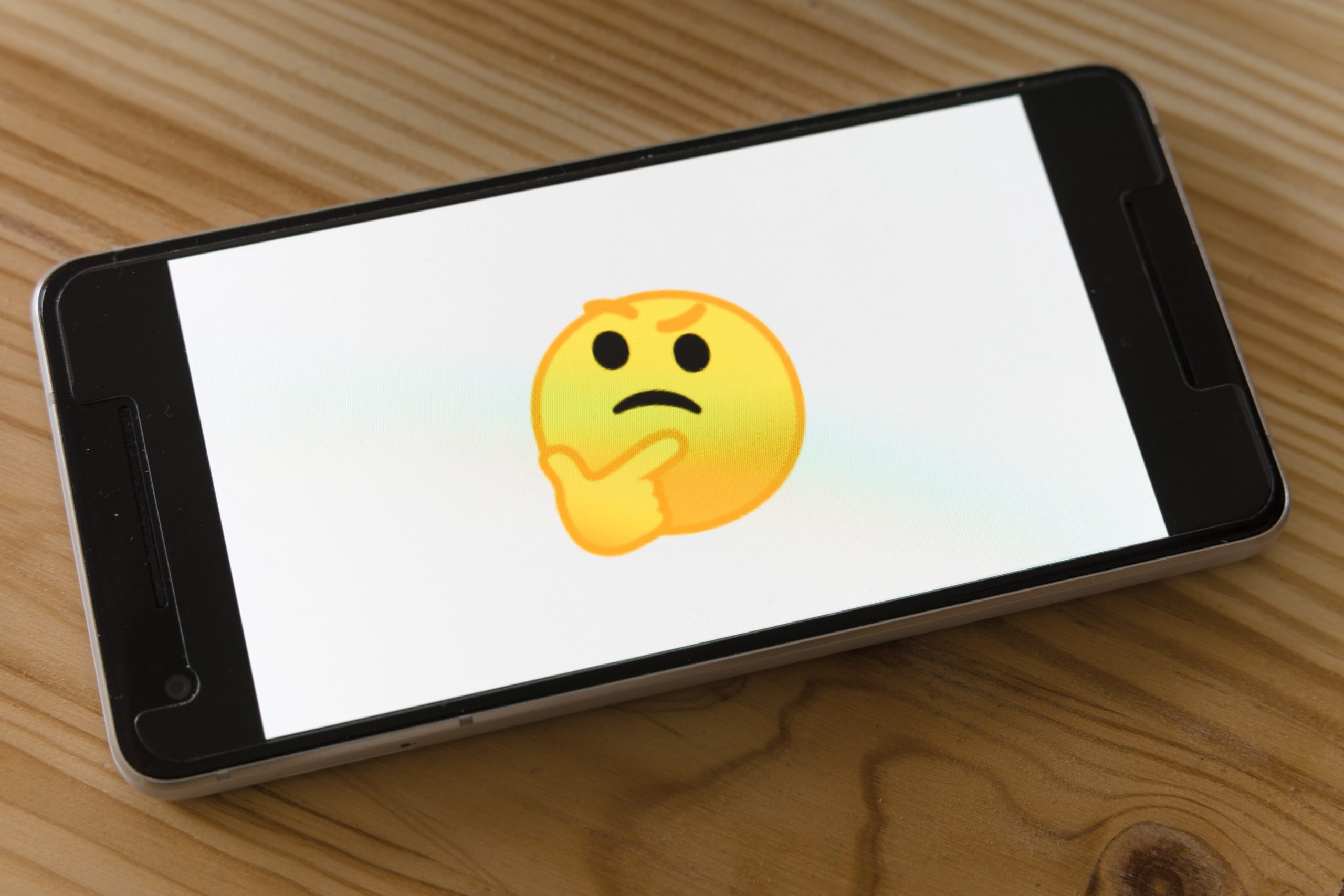 A smartphone displaying a thinking yellow emoji on the screen.