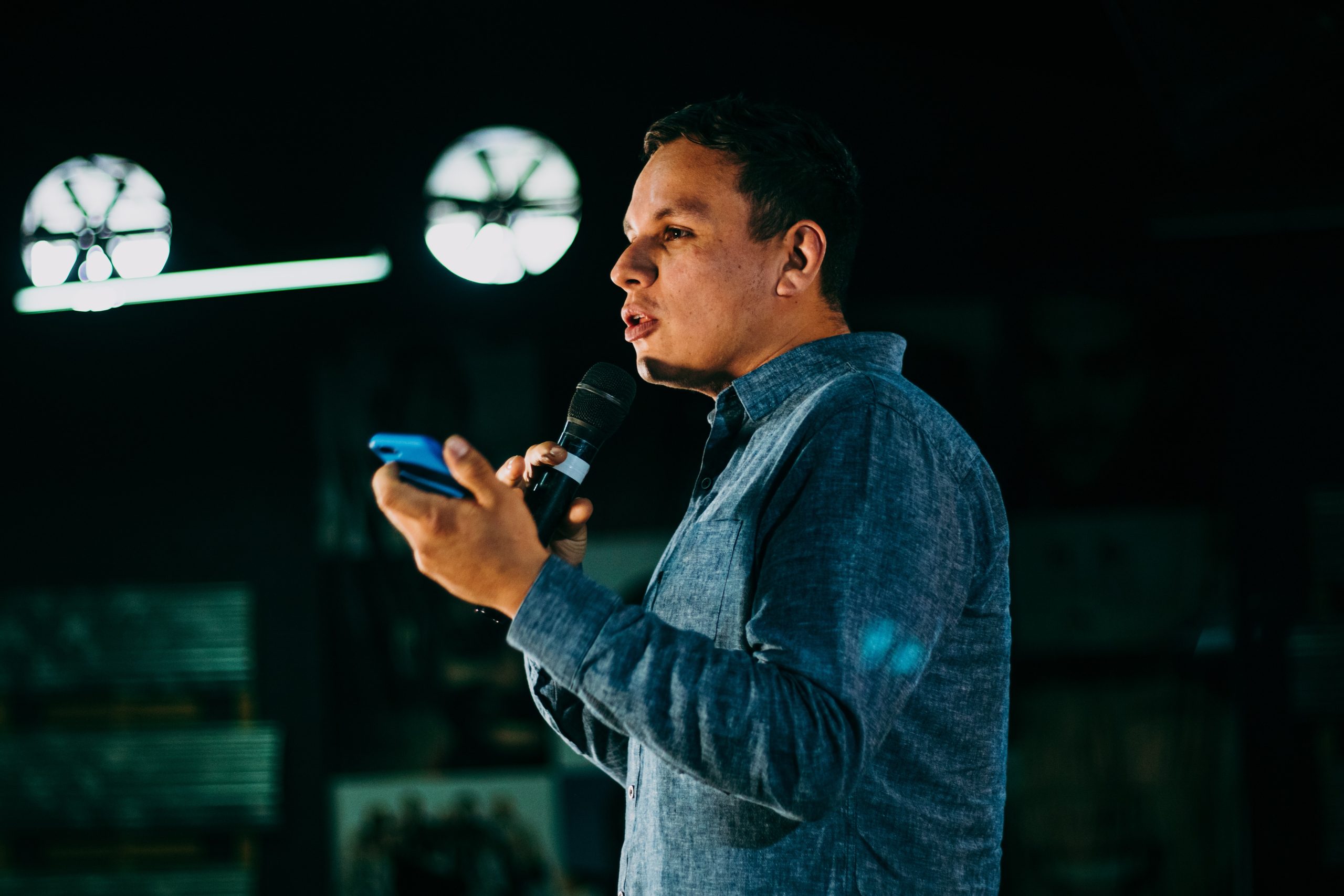 A man speaking in public and holding a phone on his left hand and a microphone on his right hand.