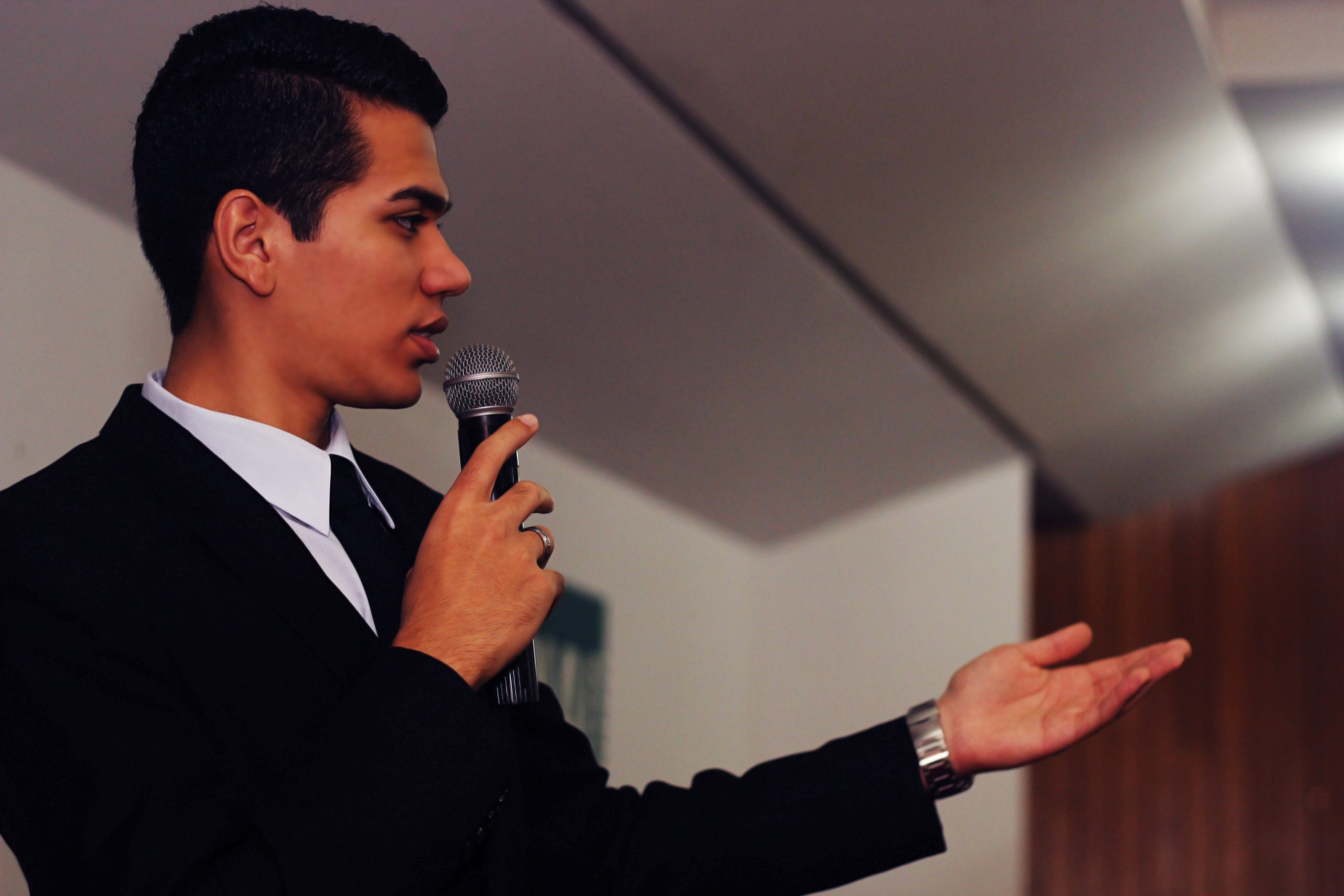 A close up of a young man wearing a suit and holding a microphone while giving a speech.