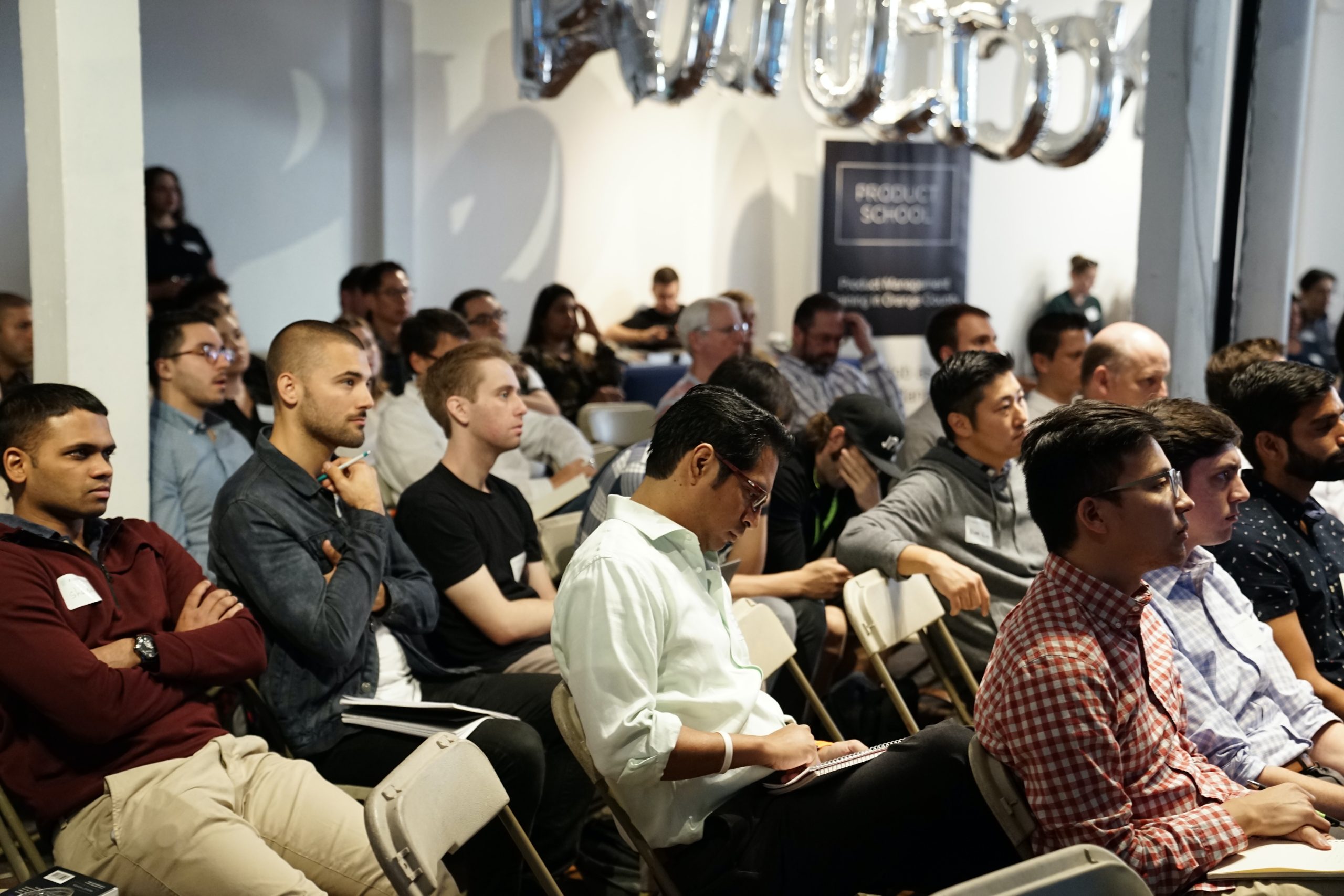 People sitting in an audience listening to a presentation at a conference.