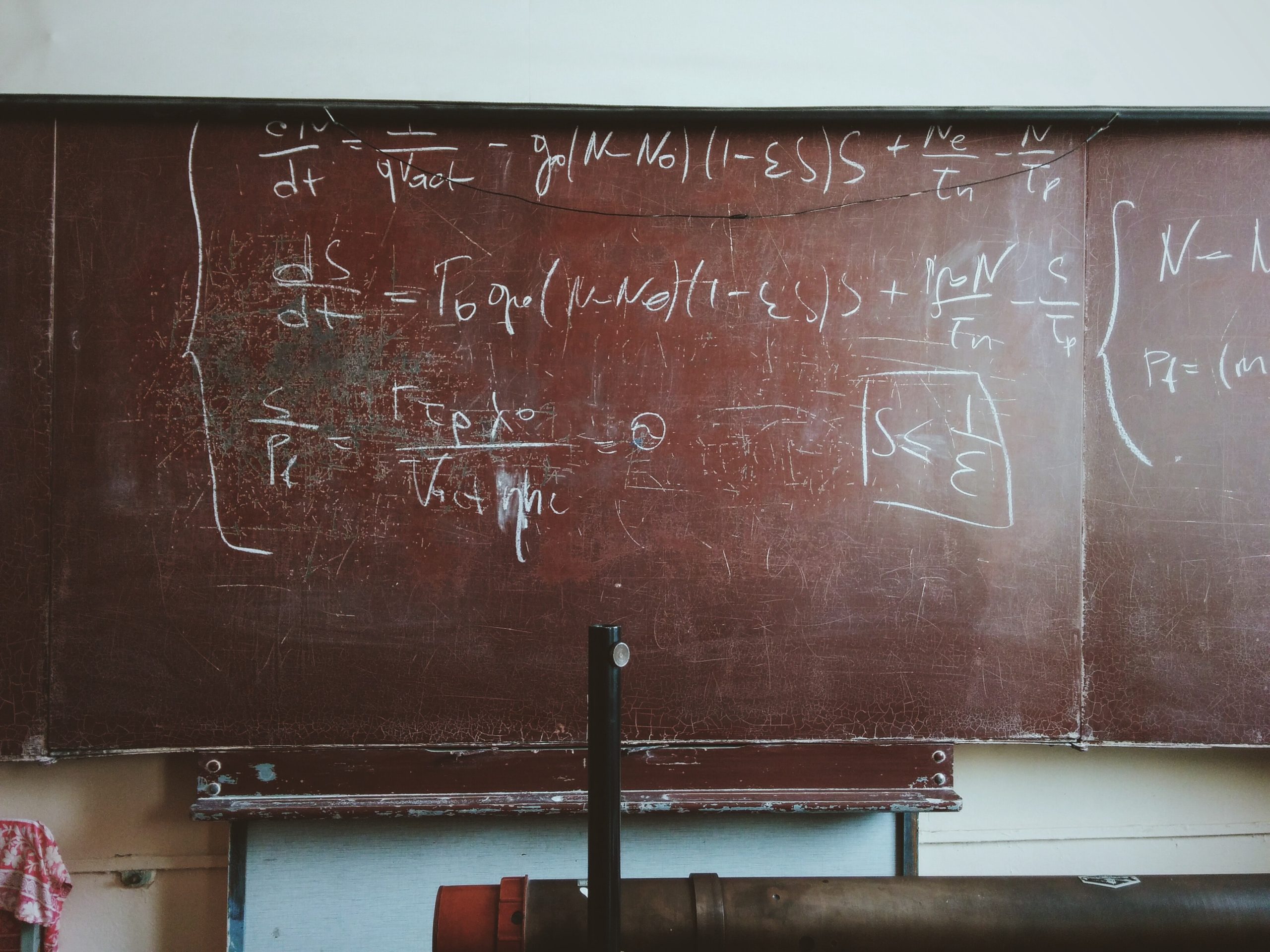 Some equations formulas written with white chalk on the old brown wooden board.