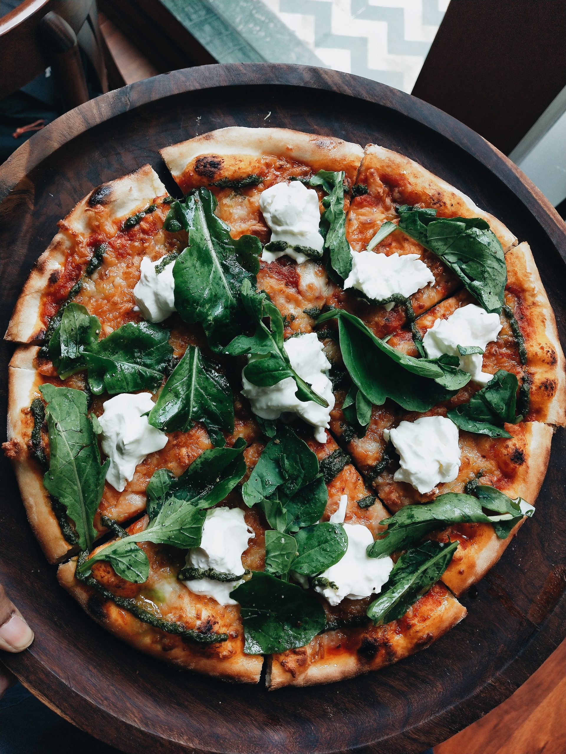 Arugula and burrata pizza with basil leaves on top.