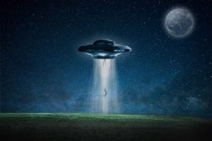 An alien spaceship beams a person up in the middle of a grass field at night.