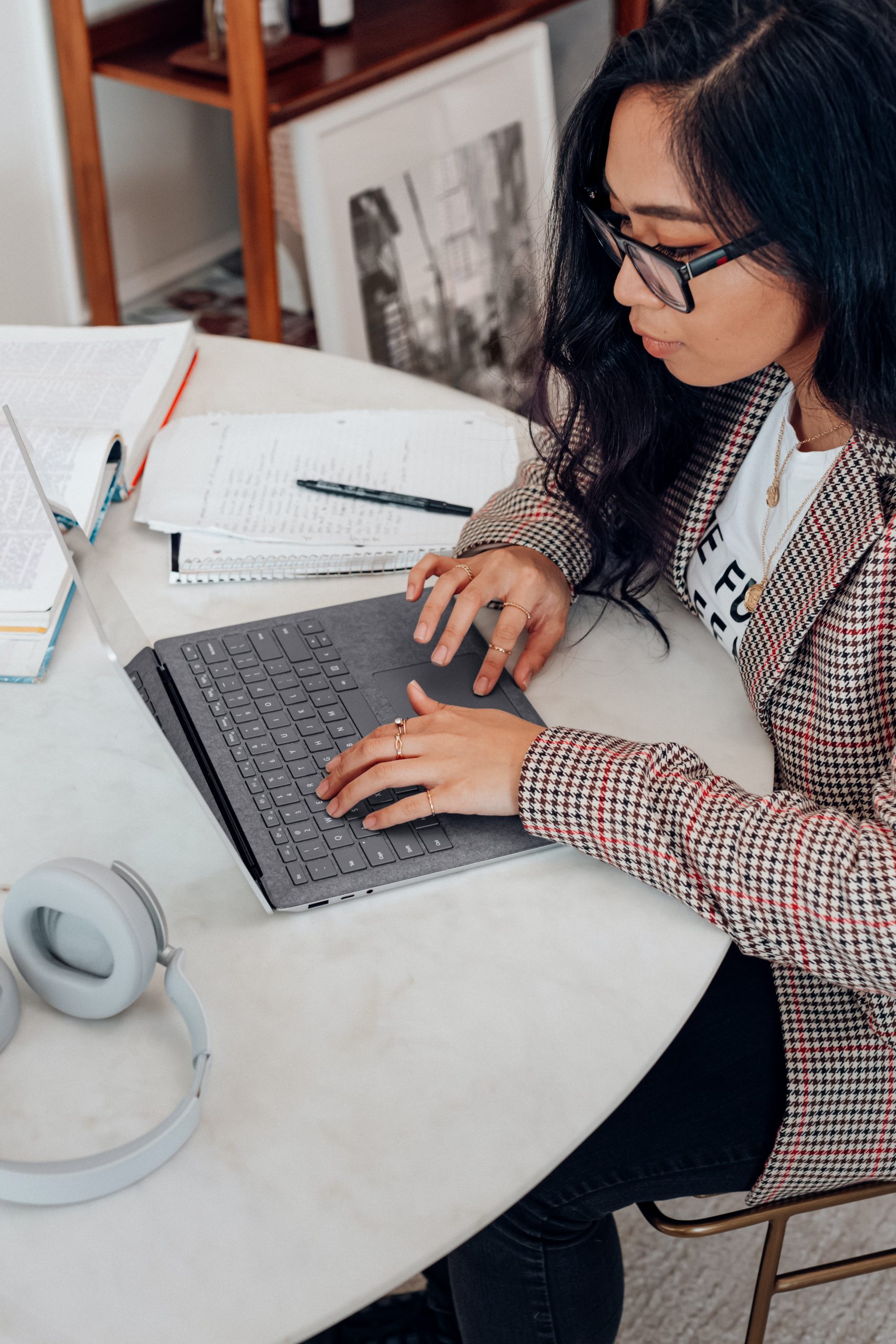 A girl typing on a computer with a notebook next to her.
