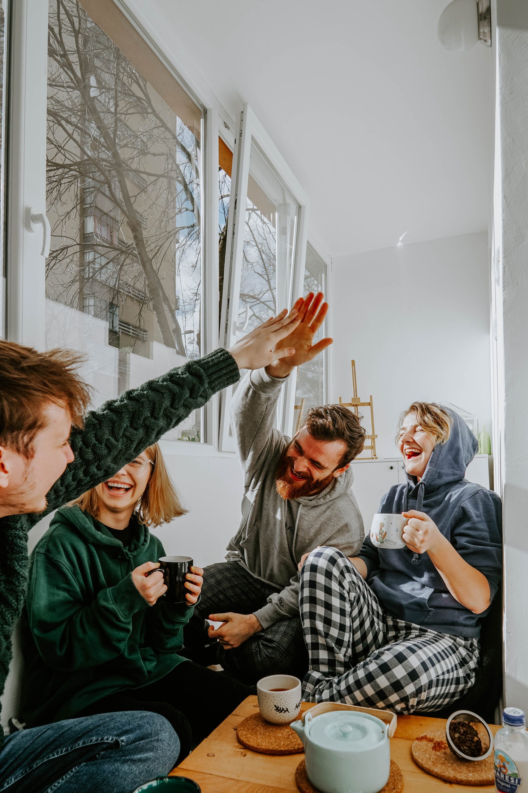 Four people are laughing and show happy faces, two girls are holding cups on each hand and two men are giving high five