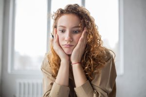 A woman holds her hands on either side of her face while looking frustrated and bored.