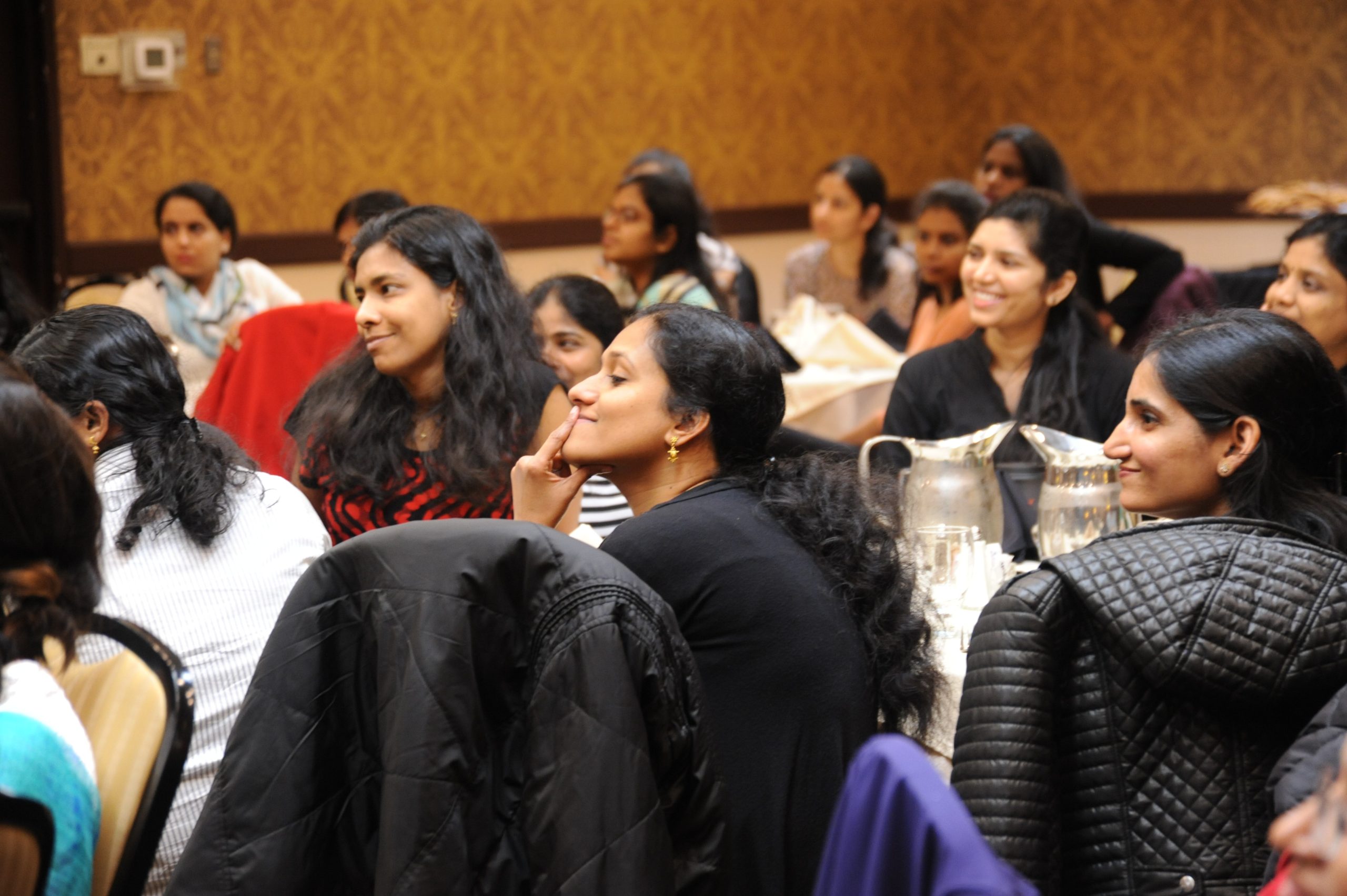 A group of women sitting on chairs while listening and some of them showing happy faces or laughing.