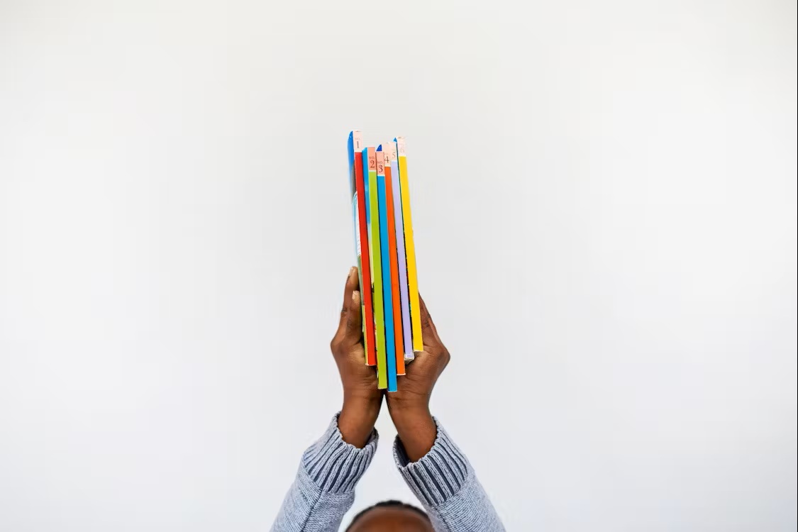 A person holding several colorful books against a white background.