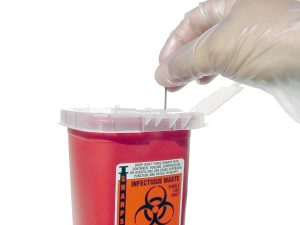 Photo showing a gloved hand placing a metal tip into a sharps container