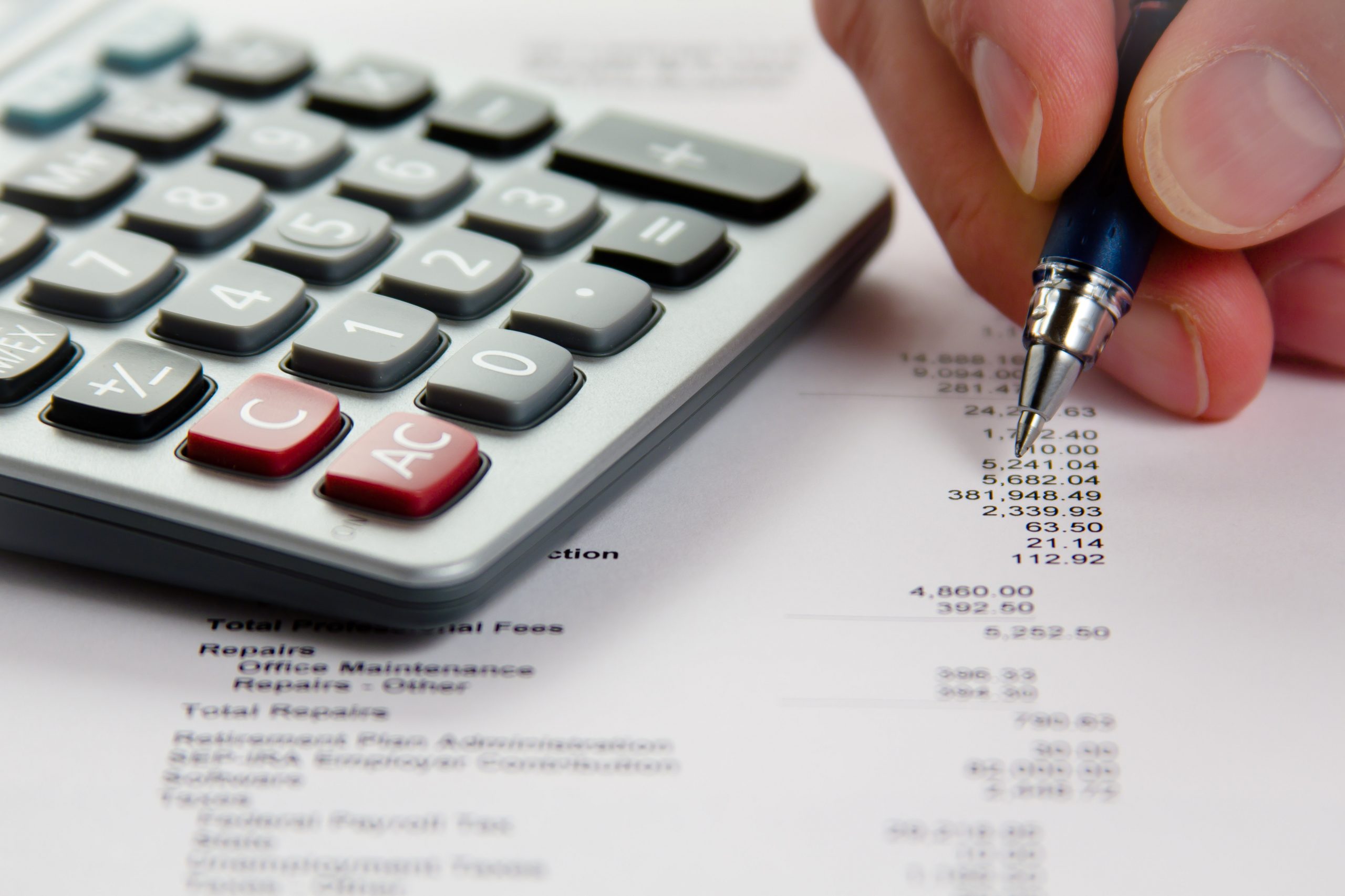 Photo showing closeup of hand holding pen over expense sheet, with calculator to side