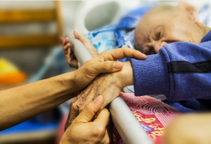 Image showing elderly man, laying in bed, holding hands of person who is out of view