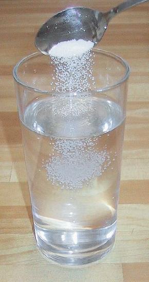 A spoon pours salt into a glass of water