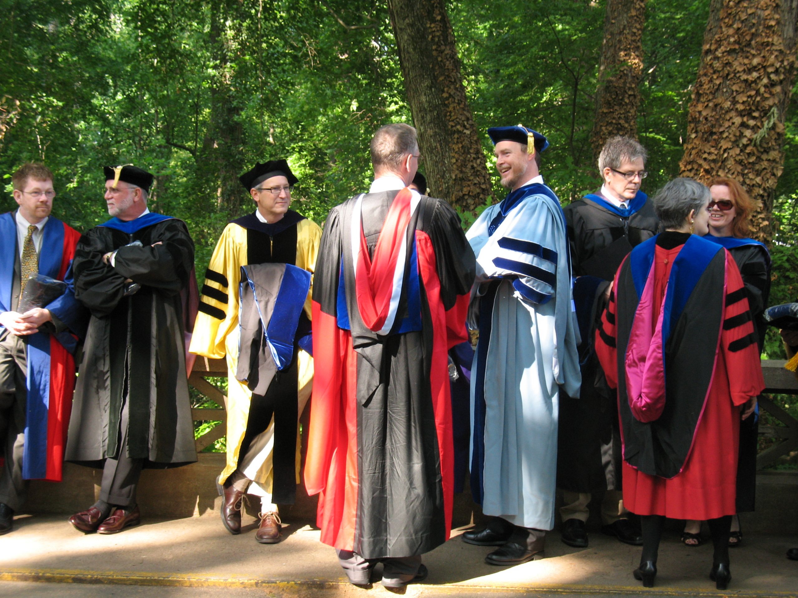 Several people in doctoral graduation robes standing outside.