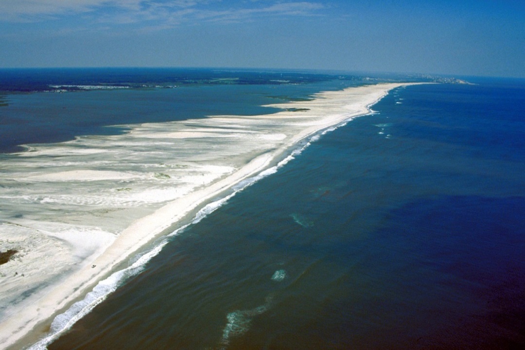 Figure 17.23 Assateague Island on the Maryland coast, U.S.A. This barrier island is about 60 km long and only 1 km to 2 km wide. The open Atlantic Ocean is to the right and the lagoon is to the left. This part of Assateague Island has recently been eroded by a tropical storm, which pushed massive amounts of sand into the lagoon. [http://soundwaves.usgs.gov/2014/04/images/DelmarvaAssateague_aerial_ViewCV.jpg]