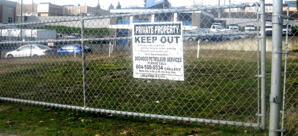 Figure 14.23 A closed and fenced gas station site in Nanaimo, B.C. The white pipes in the background are wells for monitoring groundwater contamination on the site. [SE]